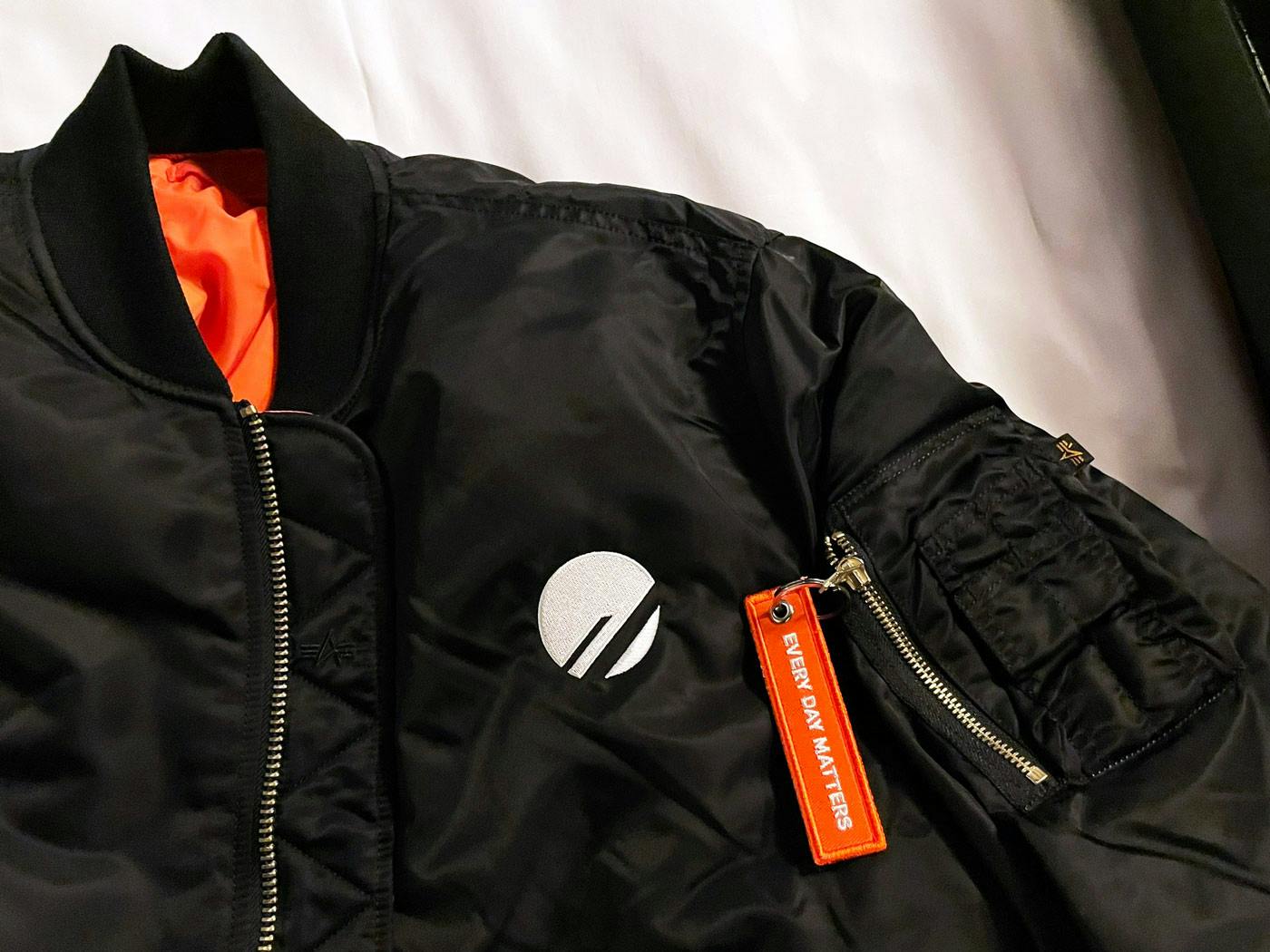 Black flight jacket with orange lining, PlanetScale logo embroidery, and orange zipper pull tag reading “Every day matters”